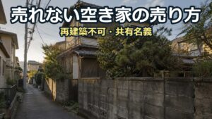 狭い道に面して建つ、雨戸を閉めたままの古い木造2階建ての空き家。庭木が塀からはみ出している