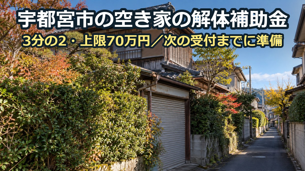 生け垣の伸びた古い木造二階建ての空き家と、その前の細い坂道。奥に住宅が続く