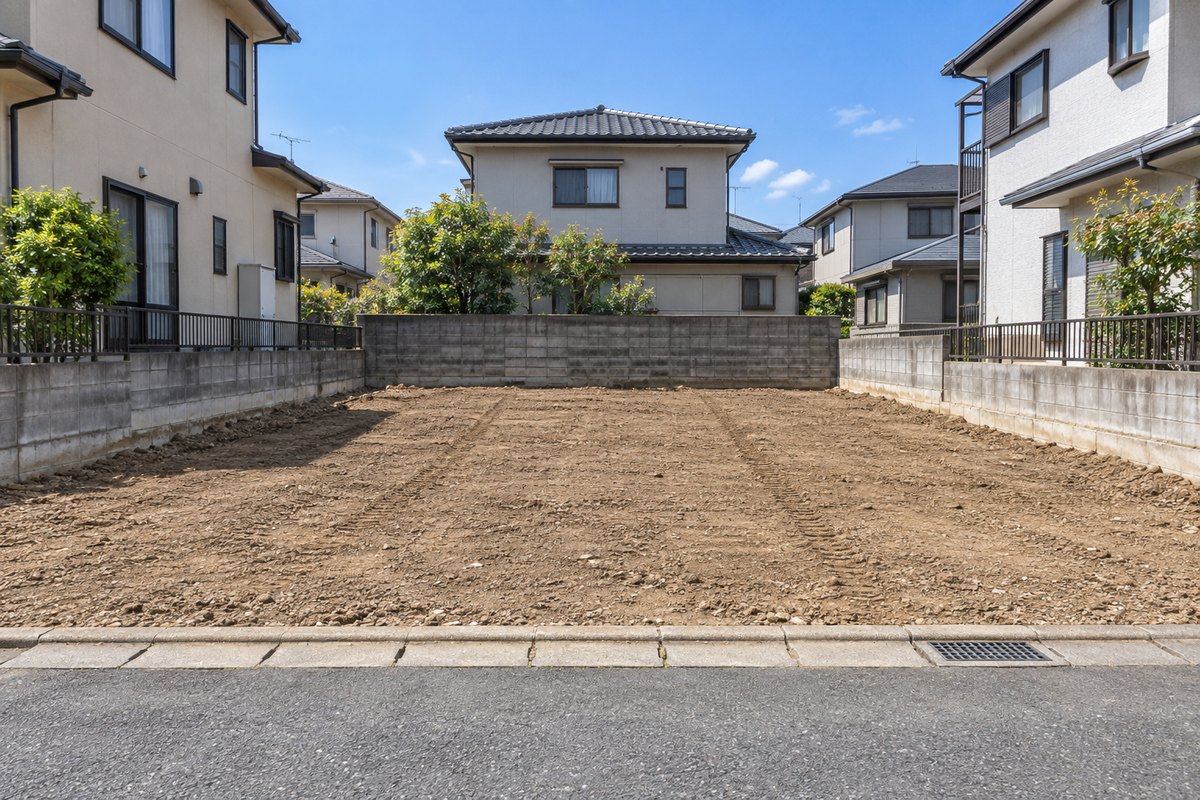 解体が終わって平らに整地された住宅地の更地。ブロック塀に囲まれ、両隣と奥に住宅が建っている