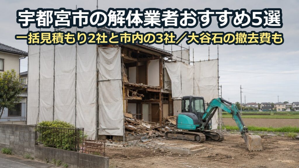 白い養生シートの足場に囲まれた木造二階建ての家を、小型の重機で解体している現場。奥に田畑と低い家並み